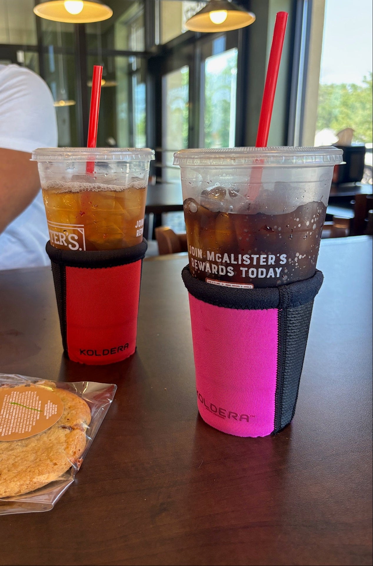 Two iced beverages with colorful sleeves on a table.