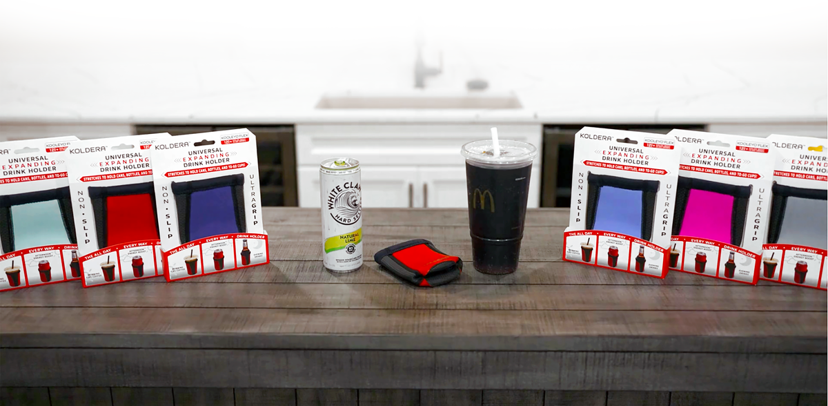 Koldera Kooleyo Flex 12 oz + universal expanding drink holder product in packaging on a wooden counter with a slim white claw can and a mcdonalds large to go soda to illustrate universal fit for every drink size